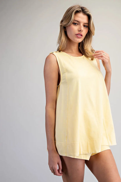 Woman wearing a light yellow sleeveless dress against a plain background