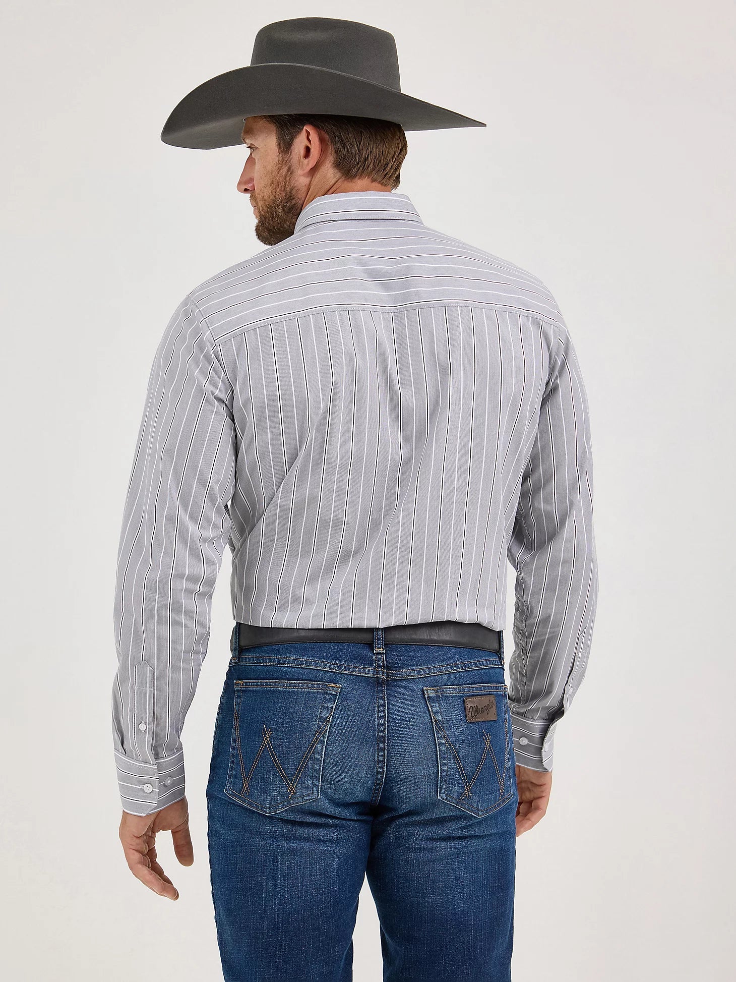Man in a gray striped western shirt, blue jeans, and cowboy hat shown from the back
