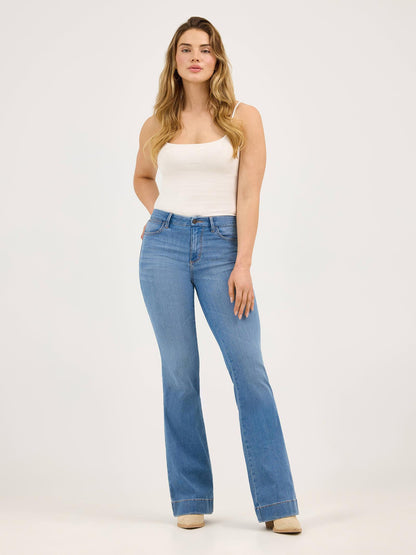 Woman wearing light blue flared jeans and white tank top on a plain background