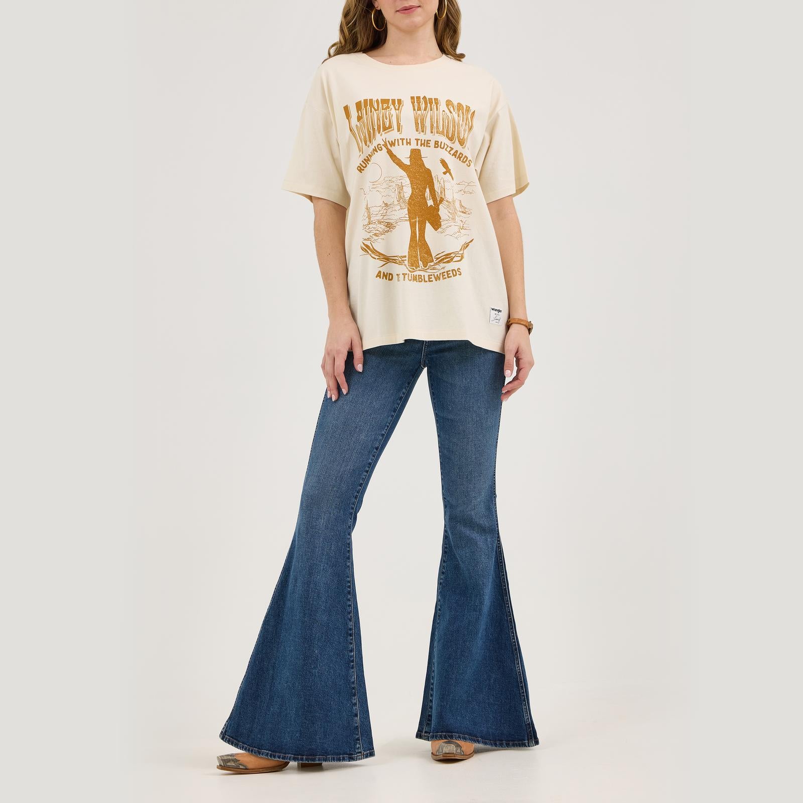 Woman wearing graphic western t-shirt and flared blue jeans on white background