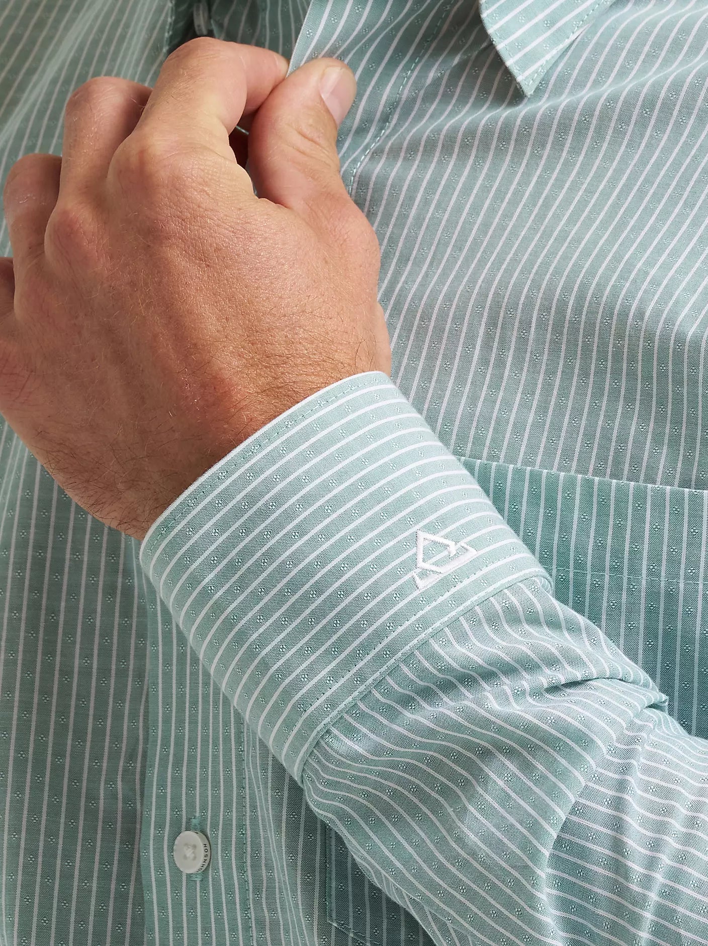 Close-up of a hand adjusting the sleeve of a green striped shirt with a brand logo.