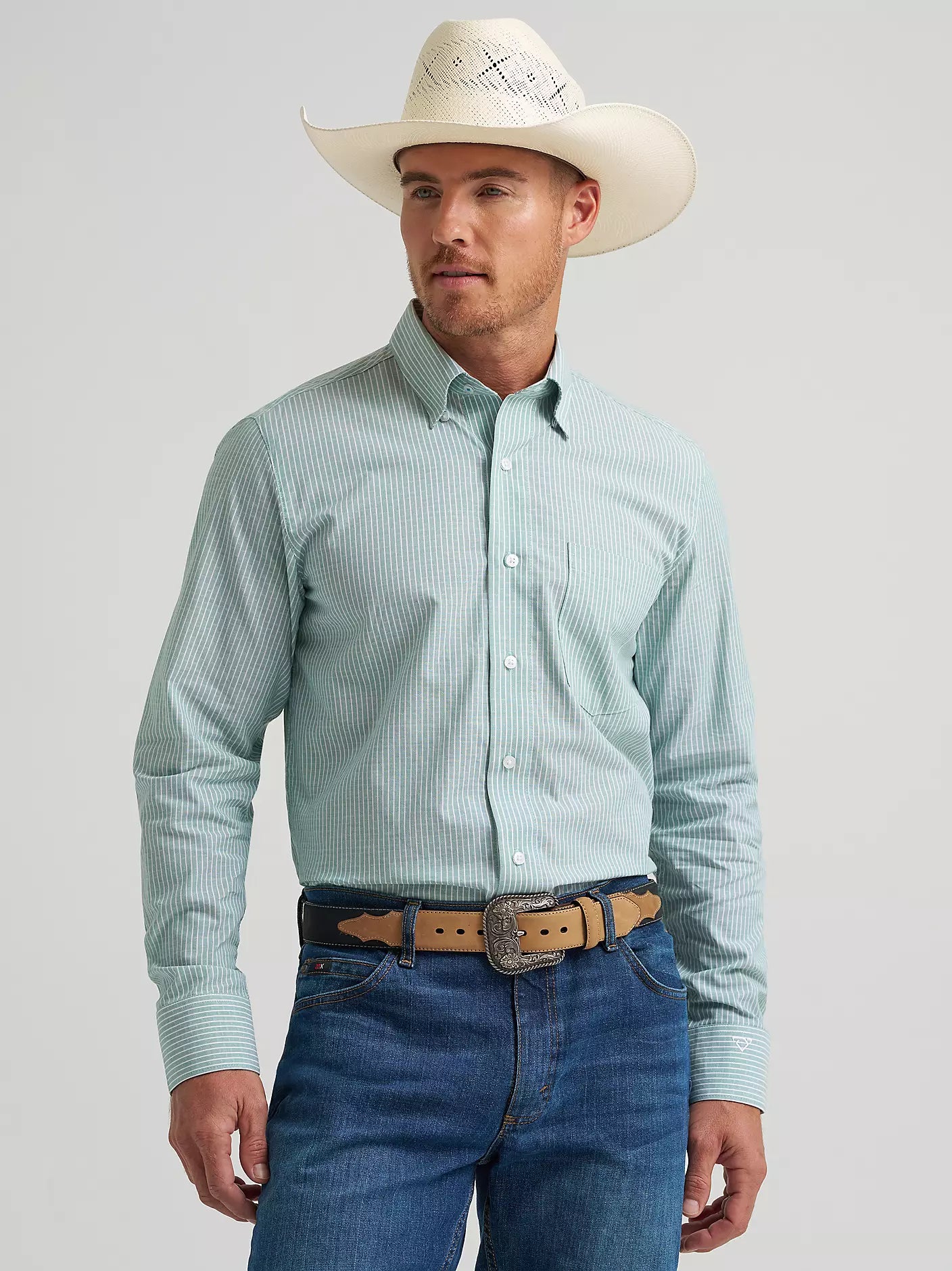 Man wearing a light blue checkered shirt, white cowboy hat, and blue jeans on a gray background