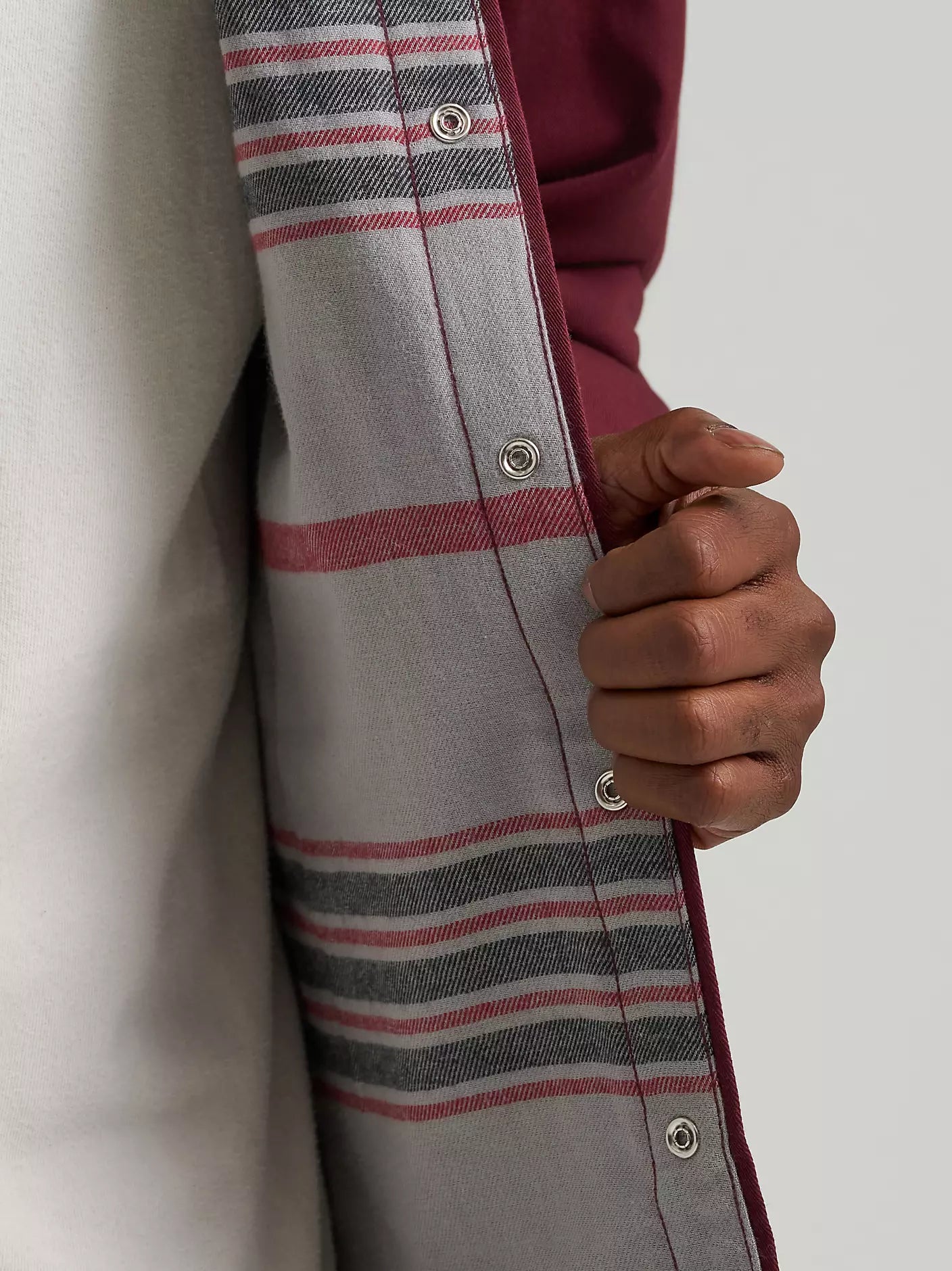 Close-up of a person wearing a gray plaid button-up shirt with red and black stripes, holding the open front to reveal a burgundy inner layer or lining.