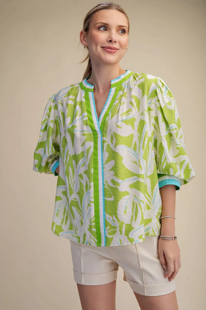 Woman wearing a green and white patterned shirt with beige shorts on a beige background