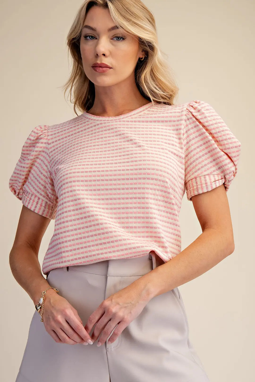 Woman wearing a pink and white striped blouse with puffed sleeves on a beige background