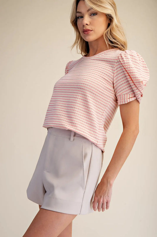 Woman wearing a pink striped top and beige shorts on a plain background