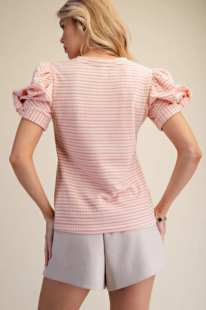 Woman wearing a pink and white striped shirt with ruffled sleeves and light gray shorts on a beige background