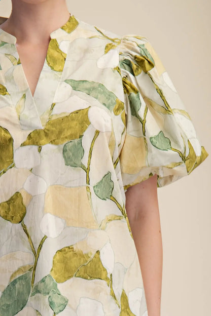 Close-up of a person wearing a white dress with green leaf patterns on a beige background