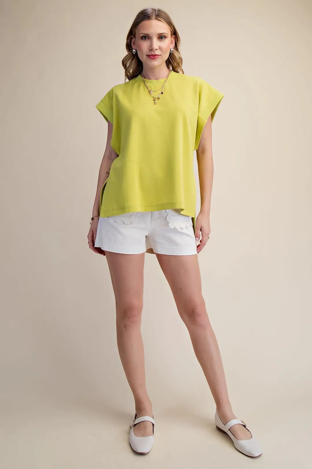 Woman wearing a bright yellow top and white shorts on a beige background