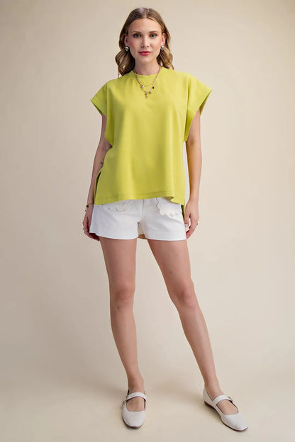 Woman wearing a bright yellow top and white shorts on a beige background
