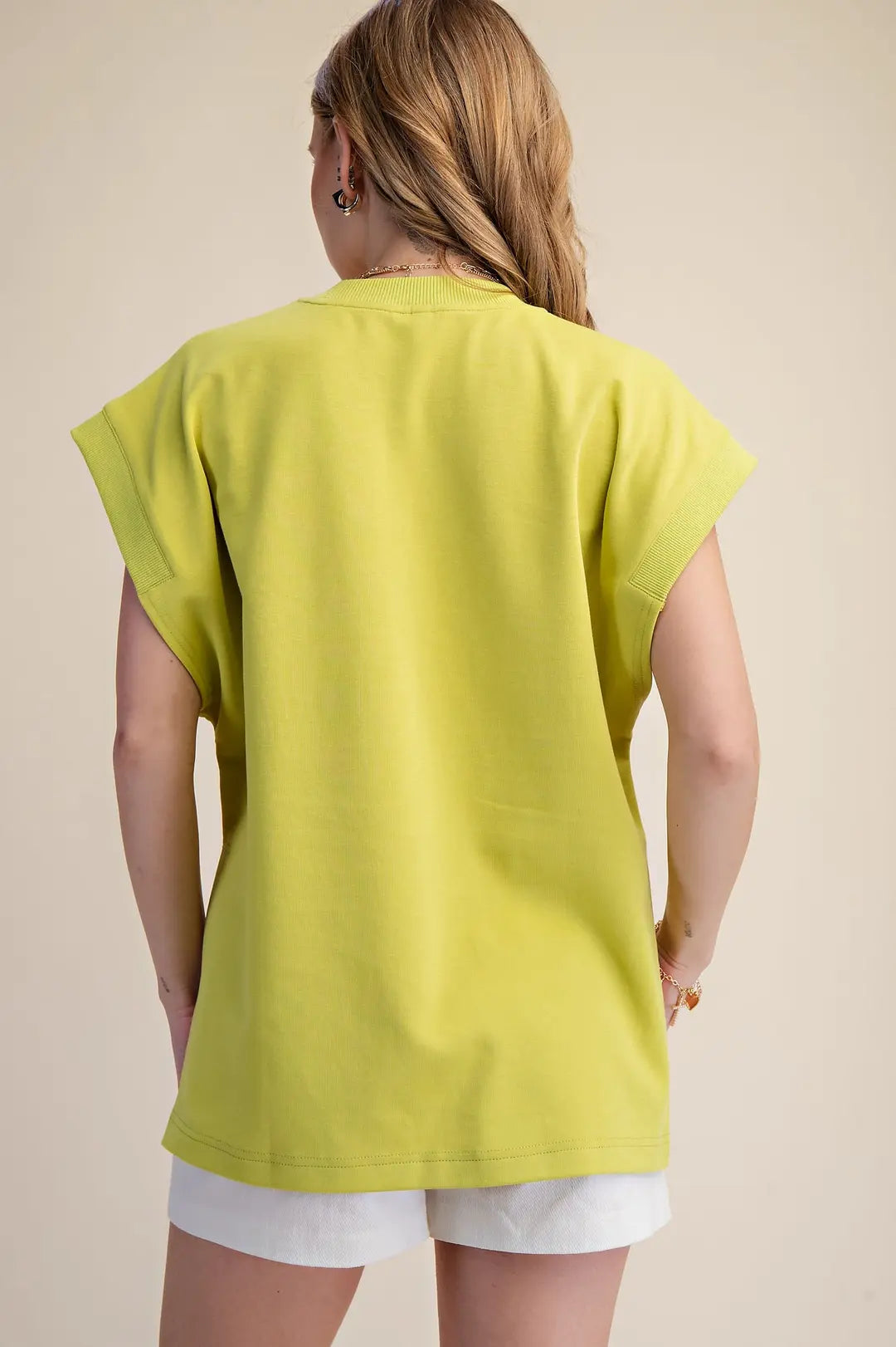 Person wearing a bright green tunic over white shorts on a beige background