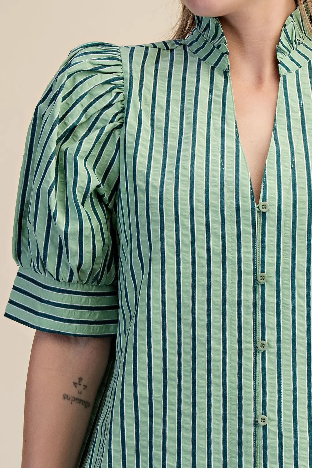 Green and blue striped shirt worn by a person on a beige background