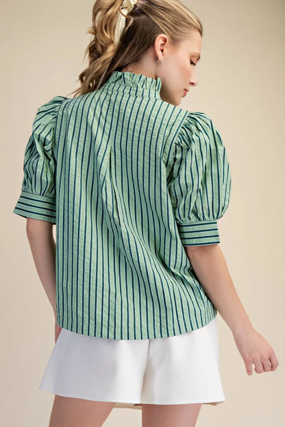 Woman wearing a green and white striped shirt with puffed sleeves on a beige background