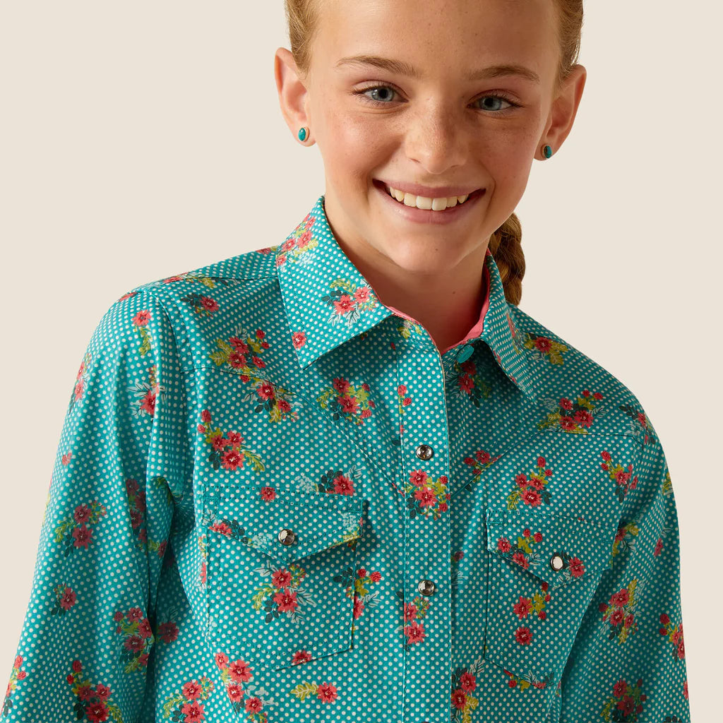 Girl wearing teal floral button-up shirt with polka dots, smiling against plain background.