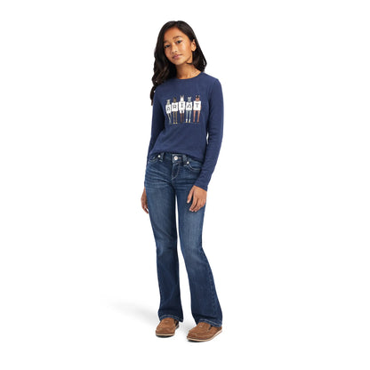 Girl in blue ARIAT graphic long sleeve shirt, bootcut jeans, and brown casual shoes.