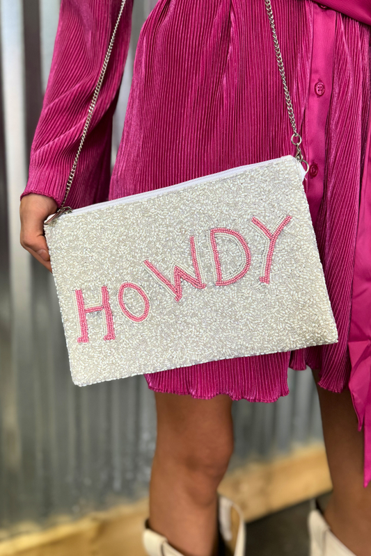 Person holding a glittery clutch bag with 'HOWDY' text in pink.
