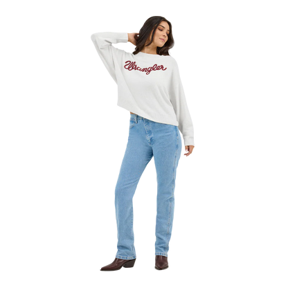 Woman wearing a white Wrangler sweater, blue high-waisted jeans, and brown boots