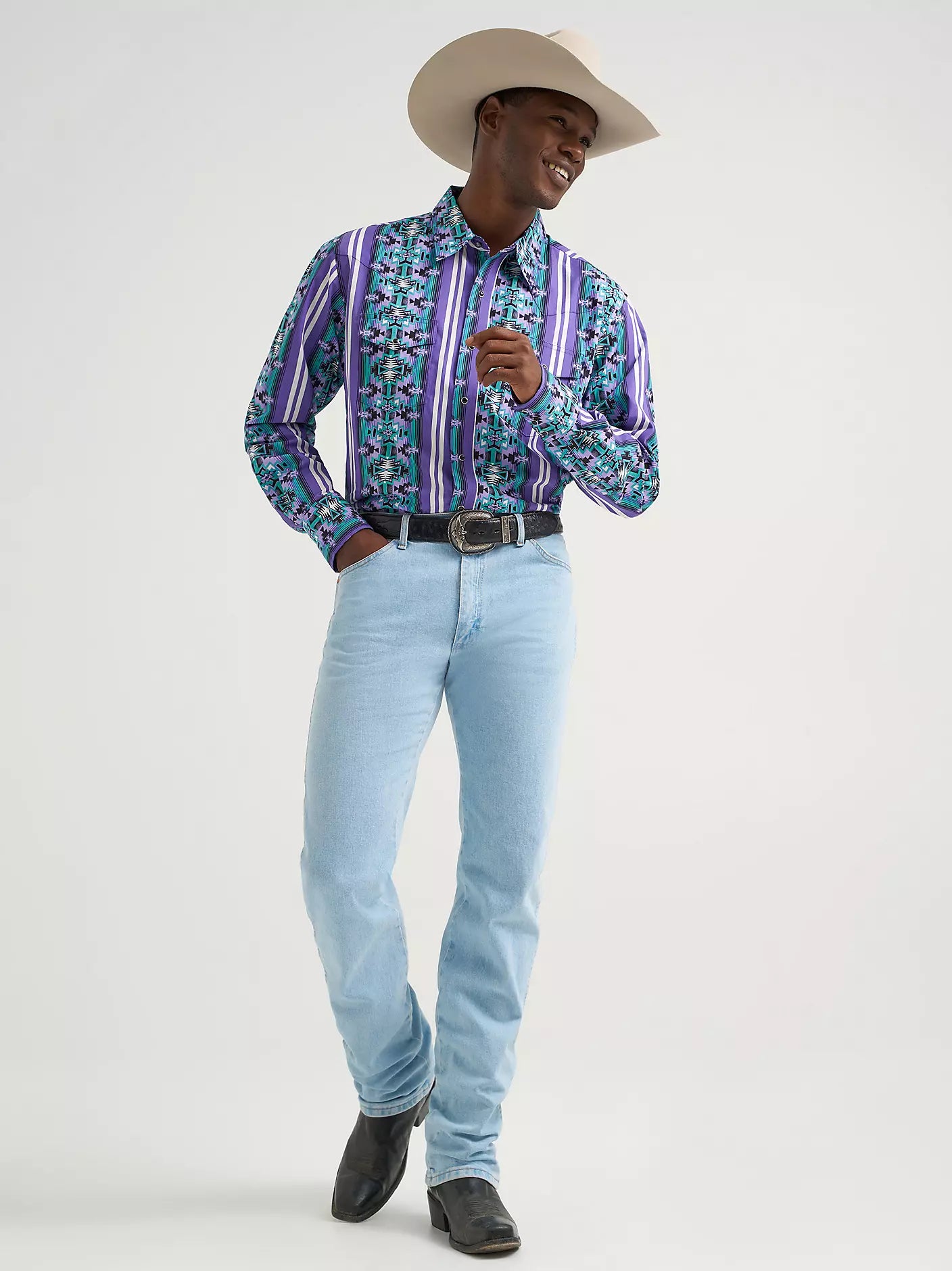 Man in cowboy hat, patterned western shirt, light blue jeans, cowboy boots, and belt buckle.
