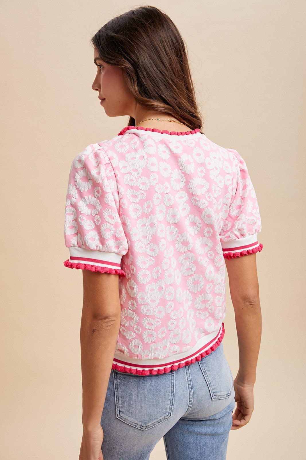 Woman wearing a pink and white patterned blouse with ruffled trim on a beige background