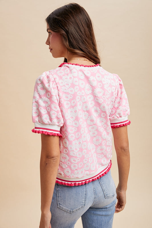 Woman wearing a pink and white patterned blouse with ruffled trim on a beige background