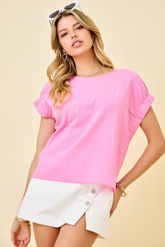 Woman wearing a pink top and white shorts against a beige background