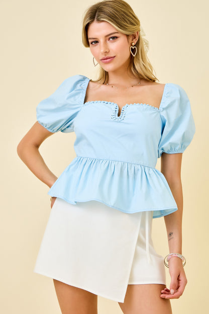 Woman wearing a light blue top with puff sleeves and a white skirt on a beige background