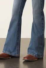 Person wearing flared blue jeans and brown cowboy boots on a dark floor