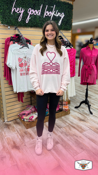 Smiling woman in casual pink graphic sweatshirt, black leggings, and sneakers standing in boutique.