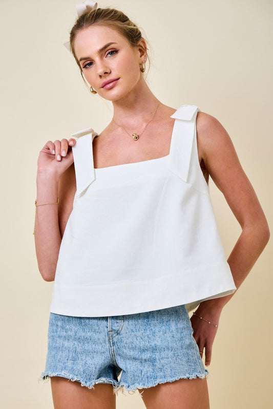 Woman wearing a white sleeveless top and denim shorts on a beige background
