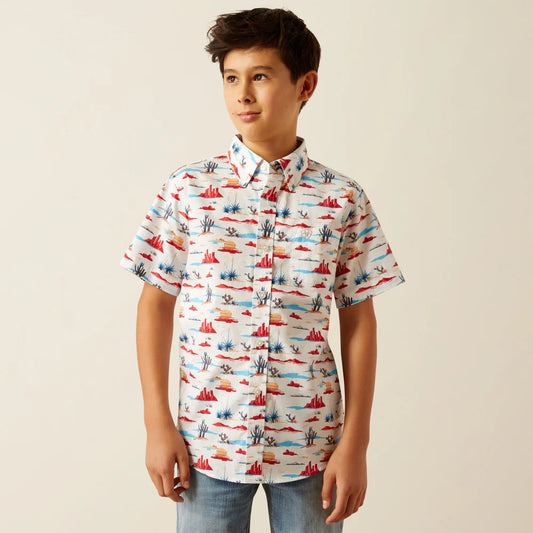 Boy wearing short sleeve desert print button-up shirt and jeans, neutral background