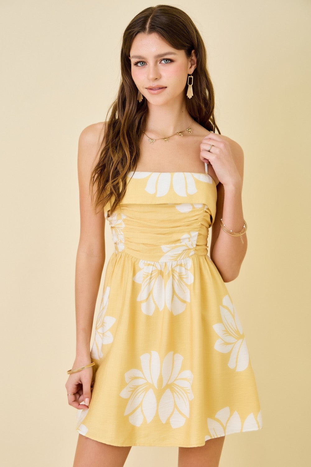Woman wearing a yellow dress with white floral patterns on a beige background
