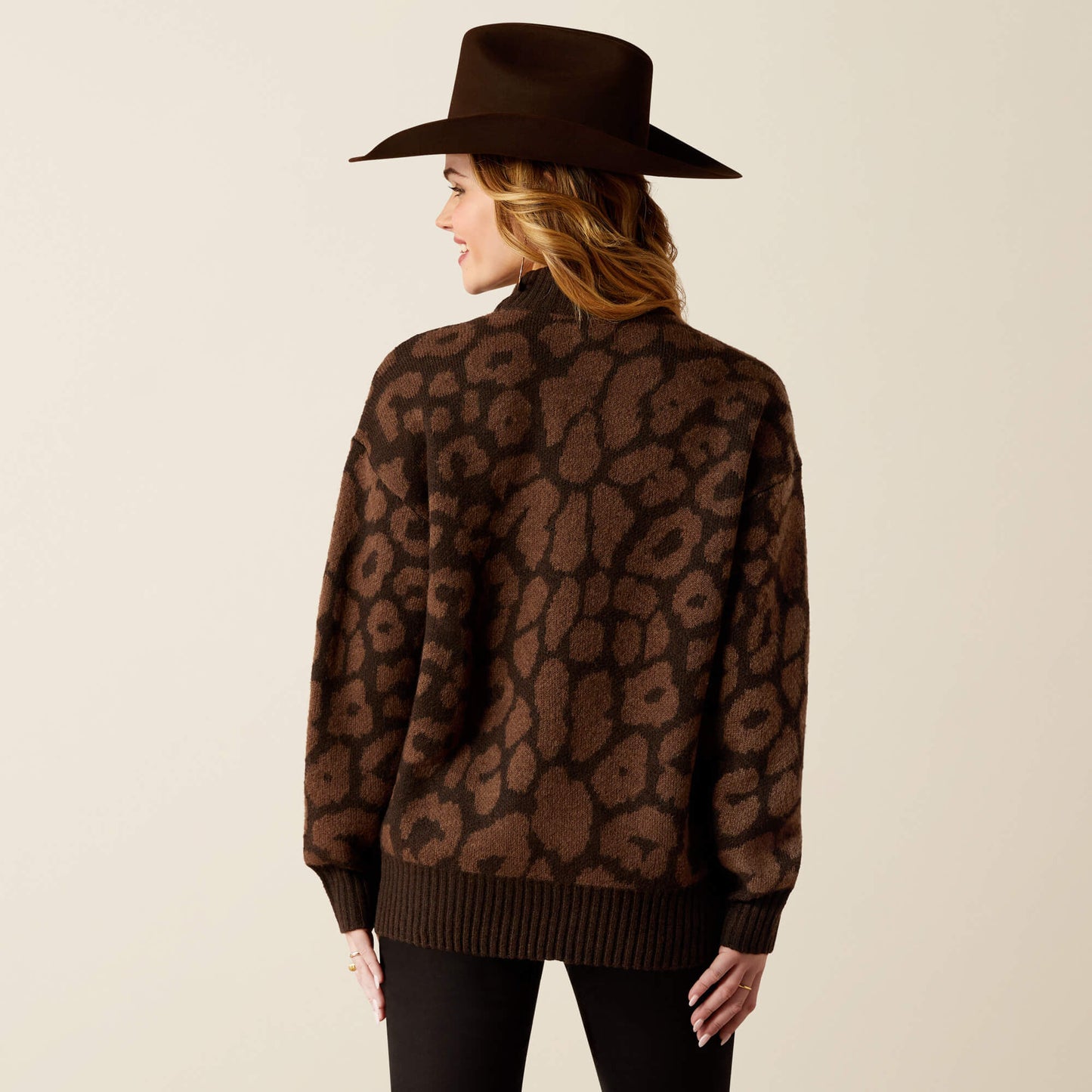 Person wearing a brown leopard print sweater and black hat on a beige background