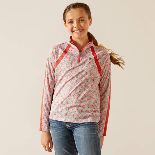 Girl wearing pink floral long sleeve shirt with red accents and blue jeans, smiling.