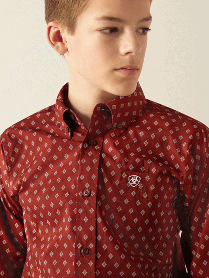 Youth in a red patterned button-up shirt with diamond print and chest pocket logo