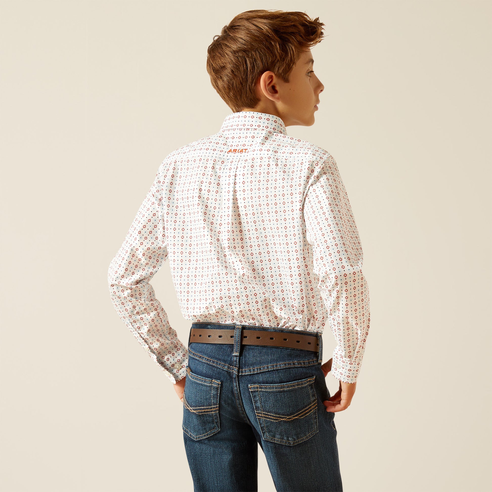 Boy wearing patterned long sleeve shirt, brown belt, and blue jeans, viewed from the back.