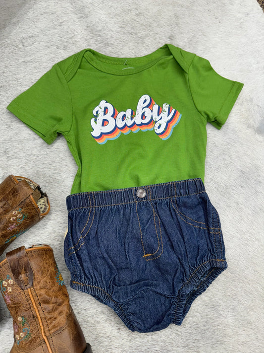 Green baby bodysuit with denim shorts and cowboy boots on a fur background