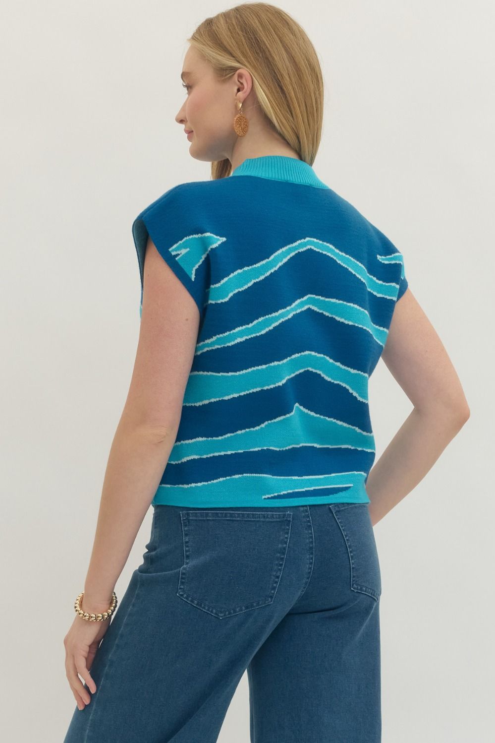 Person wearing a blue and green striped sleeveless sweater against a plain background