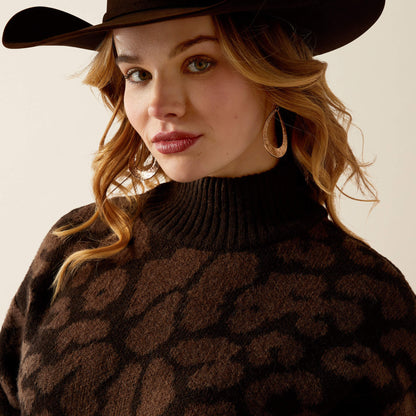 Woman wearing a brown patterned sweater and hat against a neutral background
