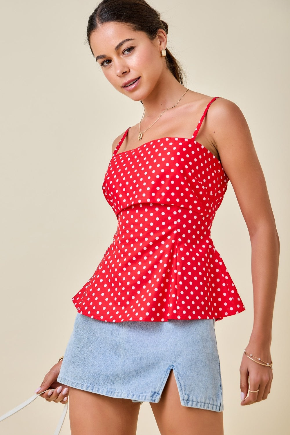 Woman wearing a red polka dot top and denim skirt on a beige background