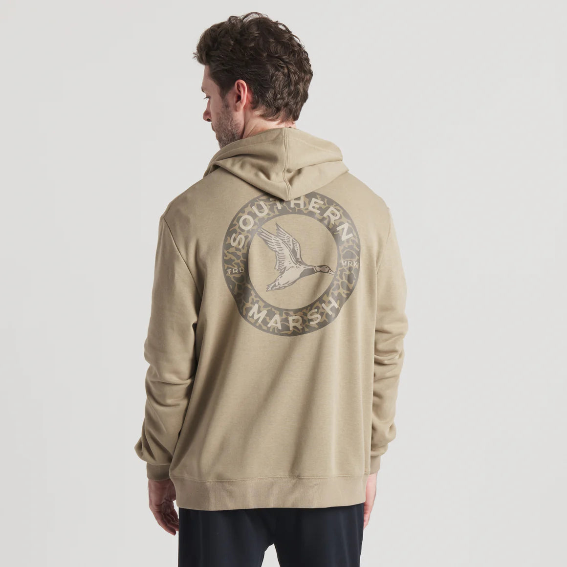 Man wearing tan hoodie with duck and Southern Marsh logo graphic on back