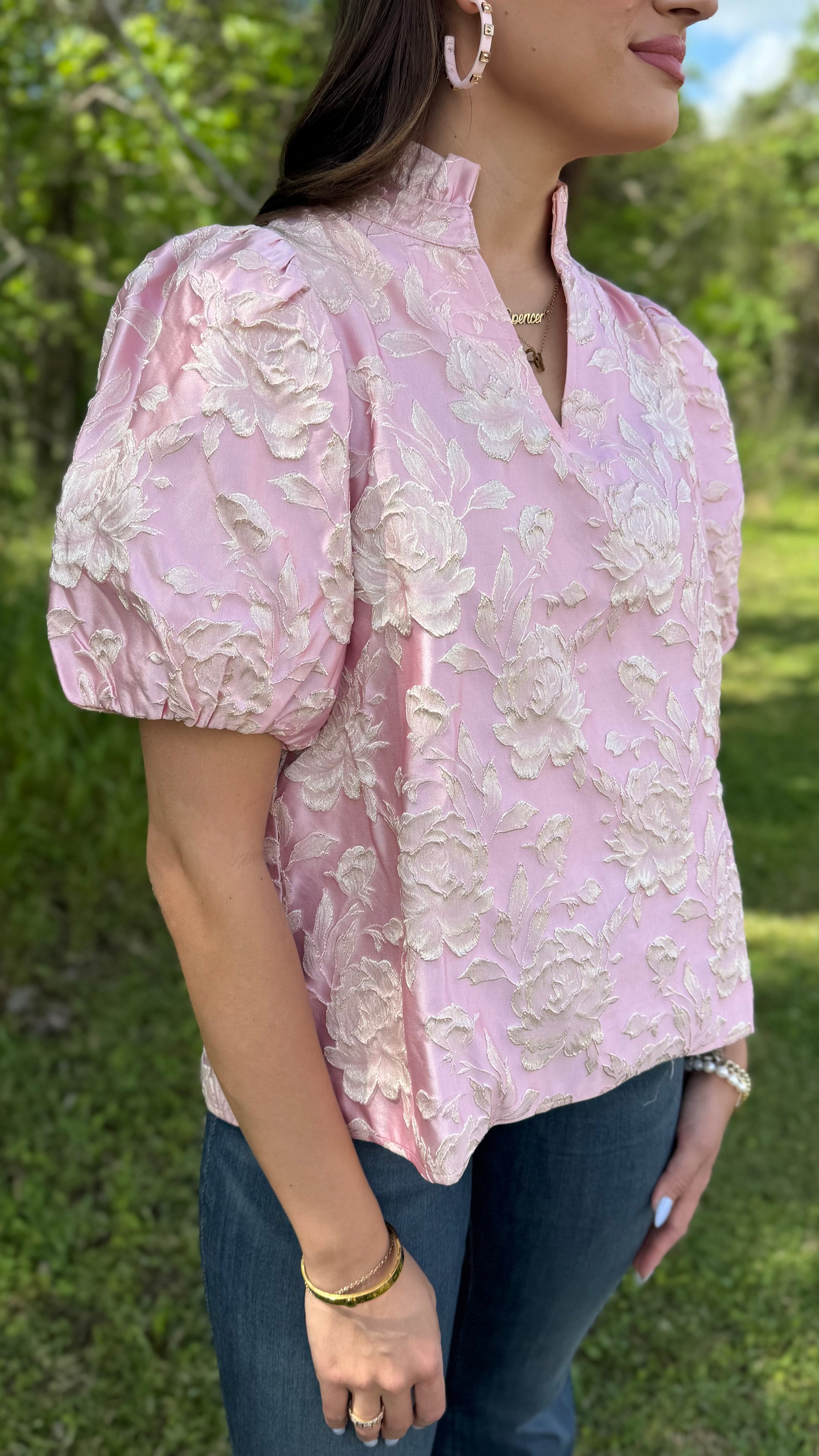 Woman wearing a pink floral blouse outdoors with greenery in the background