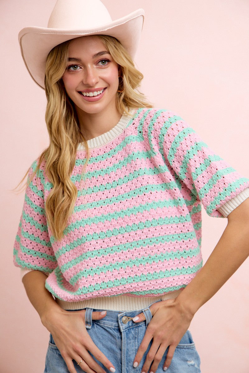 Woman wearing a pink and green striped sweater with a white cowboy hat on a pink background