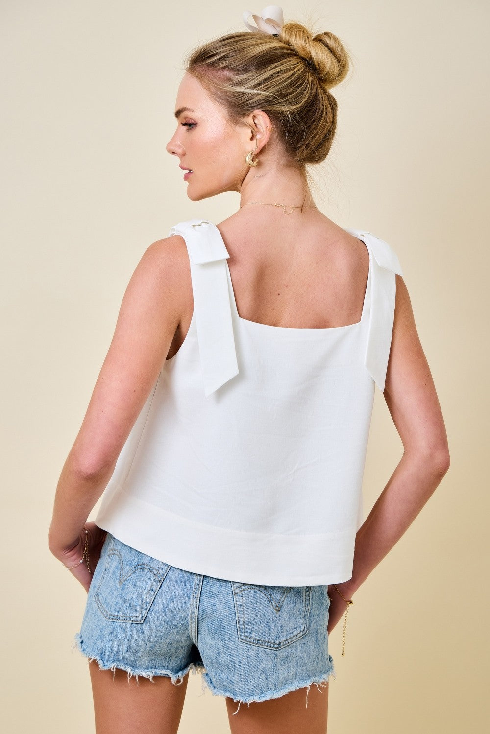 Woman wearing a white sleeveless top and denim shorts on a beige background