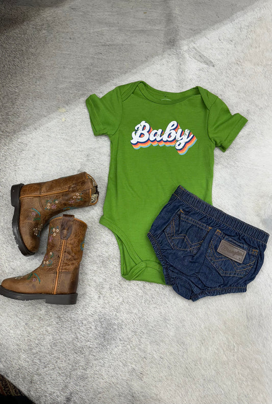Green baby onesie with 'Baby' print, denim shorts, and brown embroidered boots on fur background