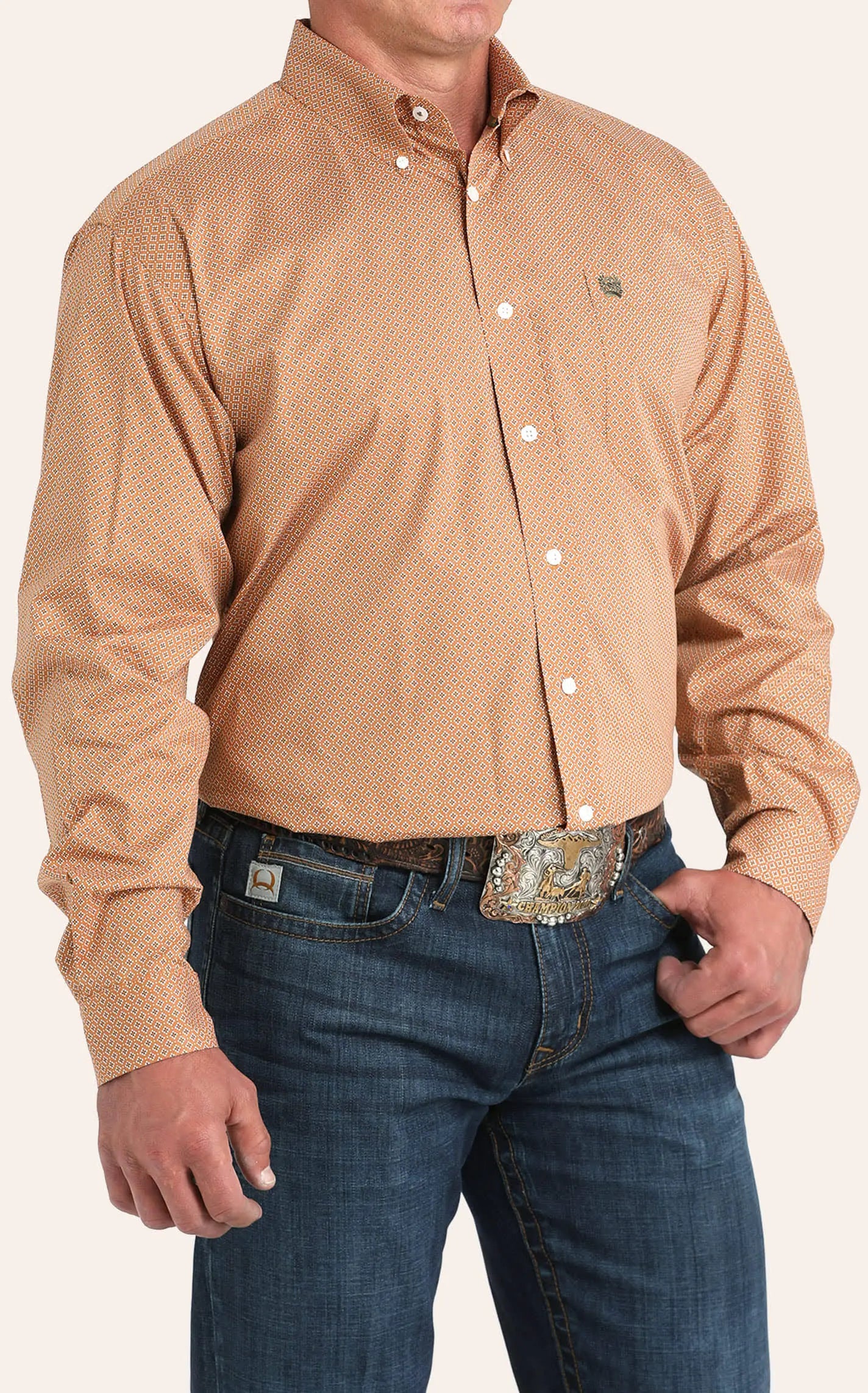 Man wearing orange geometric button-down western shirt with blue jeans and belt buckle