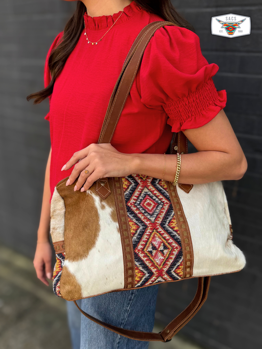 Woman carrying a leather and cowhide tote bag with colorful geometric patterns