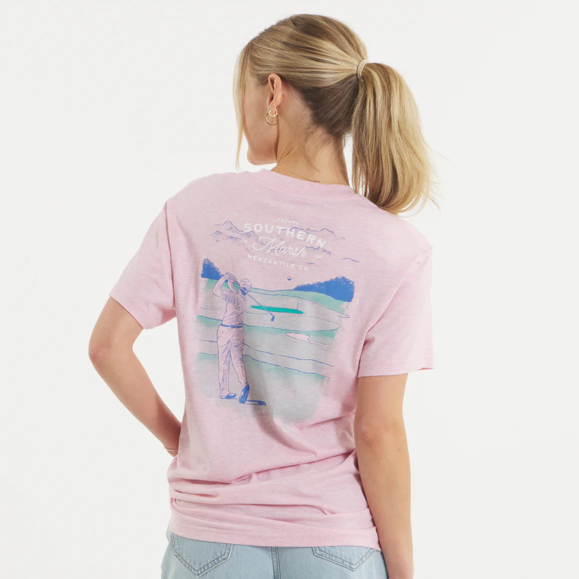 Woman in pink graphic t-shirt with golfer illustration and outdoor scene on back