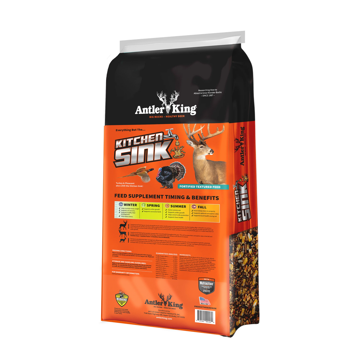A bag of Antler's King Kitchen Sink deer hunting feed supplement, featuring a black and bright orange design with illustrations of a deer, bird, and fish, and a clear window showing the granular product inside.