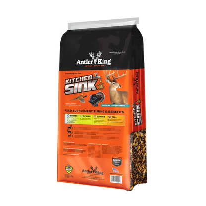 A bag of Antler's King Kitchen Sink deer hunting feed supplement, featuring a black and bright orange design with illustrations of a deer, bird, and fish, and a clear window showing the granular product inside.