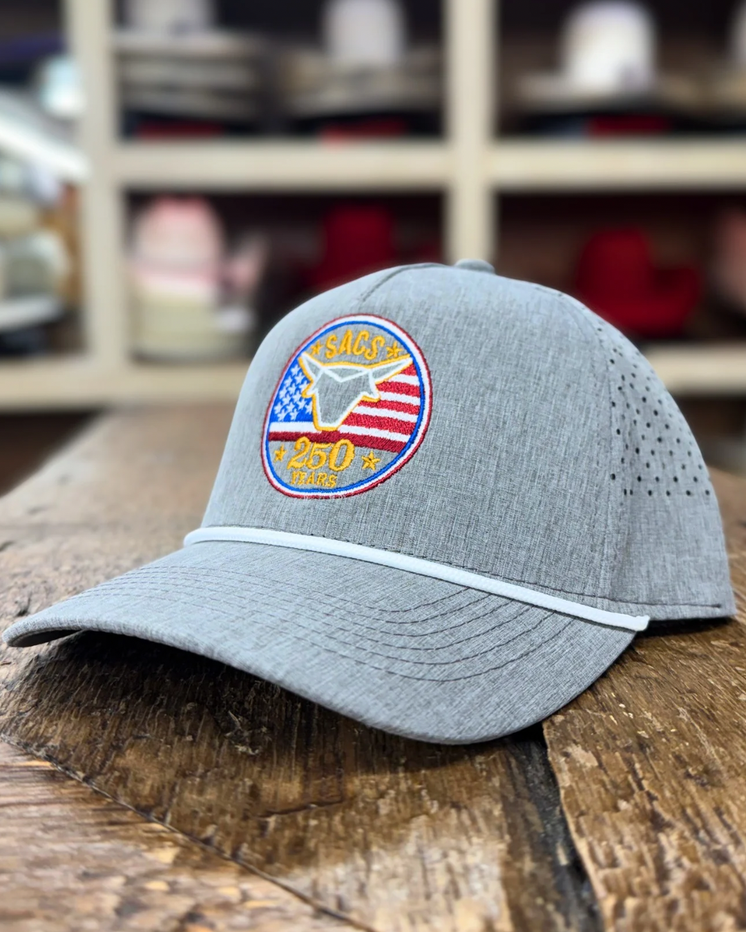 Gray cap with a logo on a wooden surface, with a blurred background of shelves with more caps.